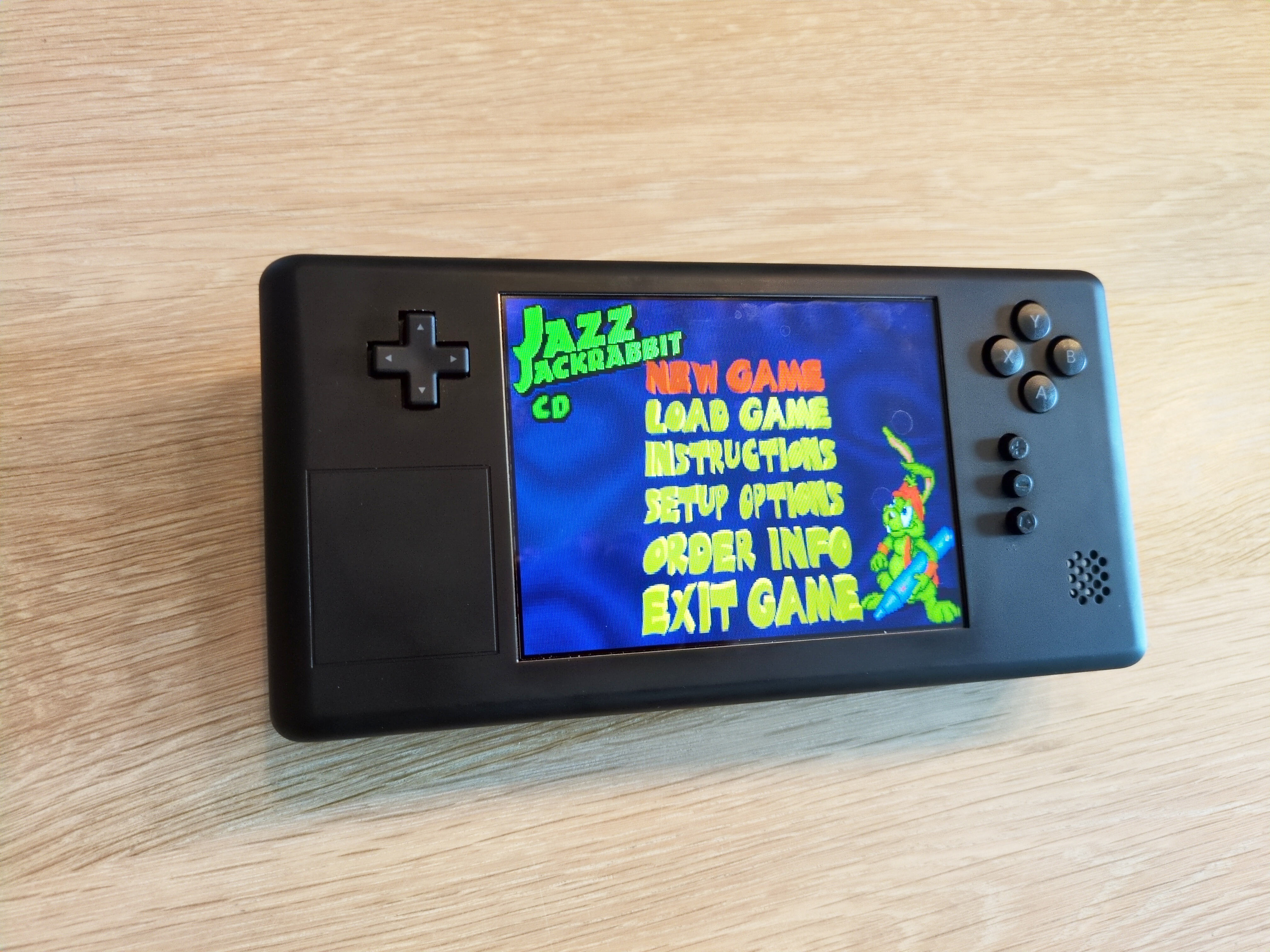 Black VapourDeck on a table. The thing has a LCD showing Jazz Jackrabbit in the middle, a D-pad on the left and XYAB and some other buttons on the right.